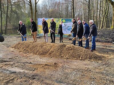 Gruppenbild: Vertreter von Wasserverband, Planungsbüro, ausführendem Unternehmen, Politik und Gemeindeverwaltung nehmen für den symbolischen ersten Spatenstich eine Schippe Sand auf.
