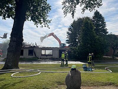 Feuerwehrleute und Bagger bei Aufräumarbeiten an der Einsatzstelle. Der Dachstuhl des ausgebrannten Gebäudes wurde inzwischen abgeräumt.