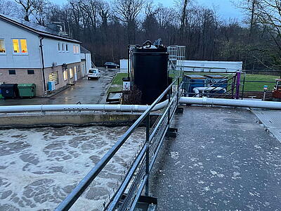 Belebungsbecken mit Ringleitung. Im Hintergrund das Gebäude der Kläranlage sowie zwei Kompressoren für die Belüftung.