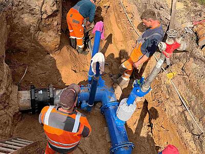 Neue Rohre und Armaturen in Baustelle mit Bauarbeitern (neuer Schieber wird eingebaut)