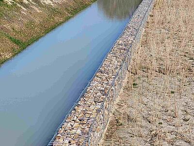 Wasser im langgestreckten Vorbecken, rechts eine Gabionenwand