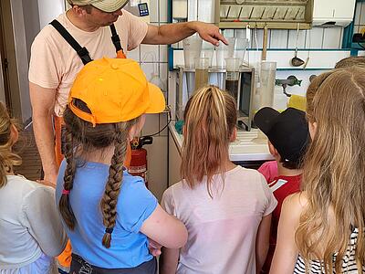 Ralf Schmieding erklärt eine Laboruntersuchung. Im Vordergrund die Kinder hören zu.