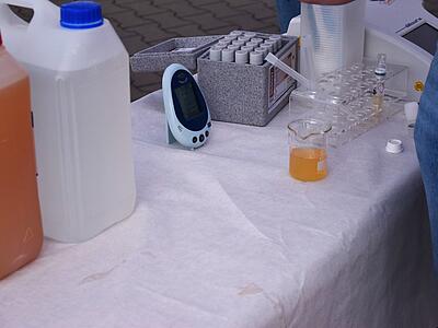 von links: Kanister mit bräunlichem Rohwasser, Kanister mit klarem Trinkwasser, Messgerät, Kästchen mit Probenbehältern, Stellage zur Lagerung von frischen Proben.