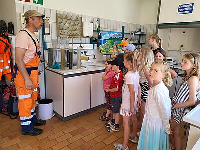 Ralf Schmieding hält einen Vortrag im Labor. Er steht links im Bild, die Kinder rechts.
