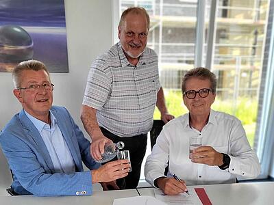 Uwe Bühning und Guido Halfter unterzeichnen, Rainer Ellermann schenkt Wasser ein.