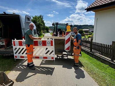 Zwei Kollegen vom Tiefbau stellen Baken auf, um die Straße zu sperren.